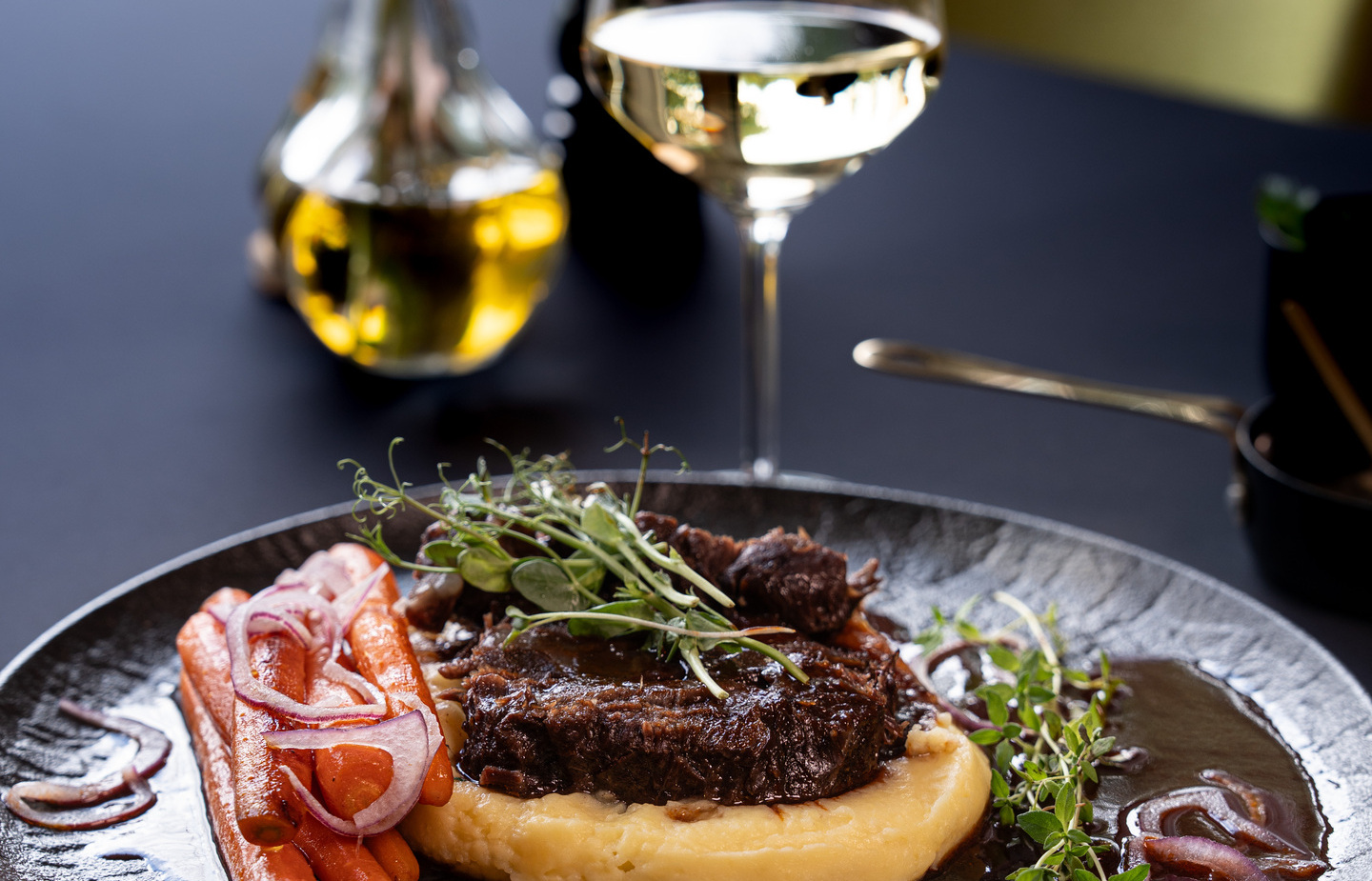 Geschmortes Rindfleisch auf Püree mit glasierten Karotten, Weißweinglas, elegante Tischdekoration