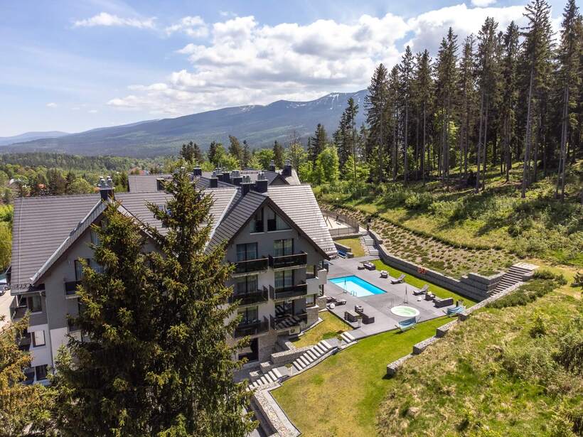Hotel with outdoor terrace featuring a pool and hot tub, surrounded by mountains and forest, modern architecture in a tranquil setting.