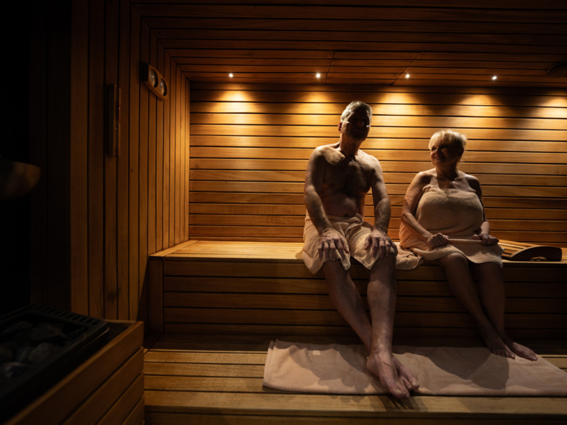 Para relaksująca się w drewnianej saunie hotelowej, otoczonej ciepłym, nastrojowym oświetleniem