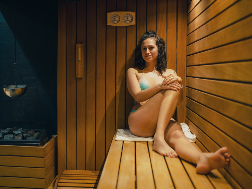 Kobieta relaksująca się w drewnianej saunie hotelowej w stroju kąpielowym, z termometrem i kamieniami do pary.