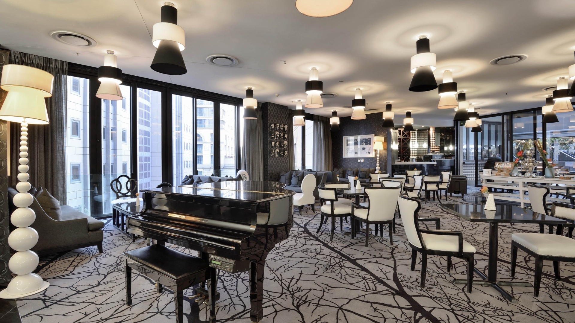 Elegant hotel lounge with a glossy grand piano, city-view floor-to-ceiling windows and modern pendant lights.