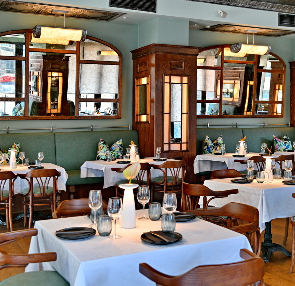 Elegante comedor de hotel con manteles blancos, sillas de madera, banqueta verde, luz cálida y espejos