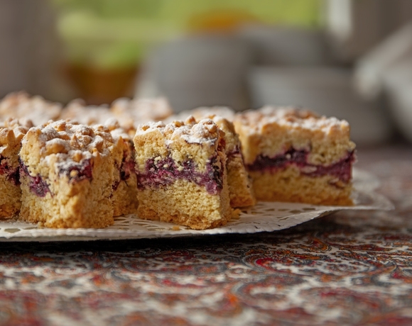 Kawałki kruchego ciasta z jagodowym nadzieniem, posypane cukrem pudrem, na paterze z serwetką na wzorzystym obrusie | wisła noclegi z wyżywieniem