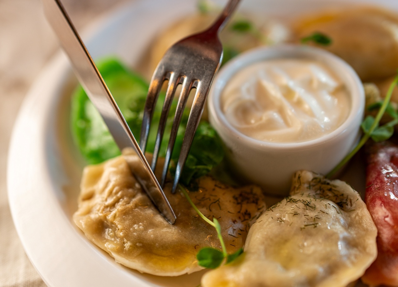 Ręka kroi pieroga na talerzu: pierogi podane z kwaśną śmietaną, koperkiem i małą sałatką.