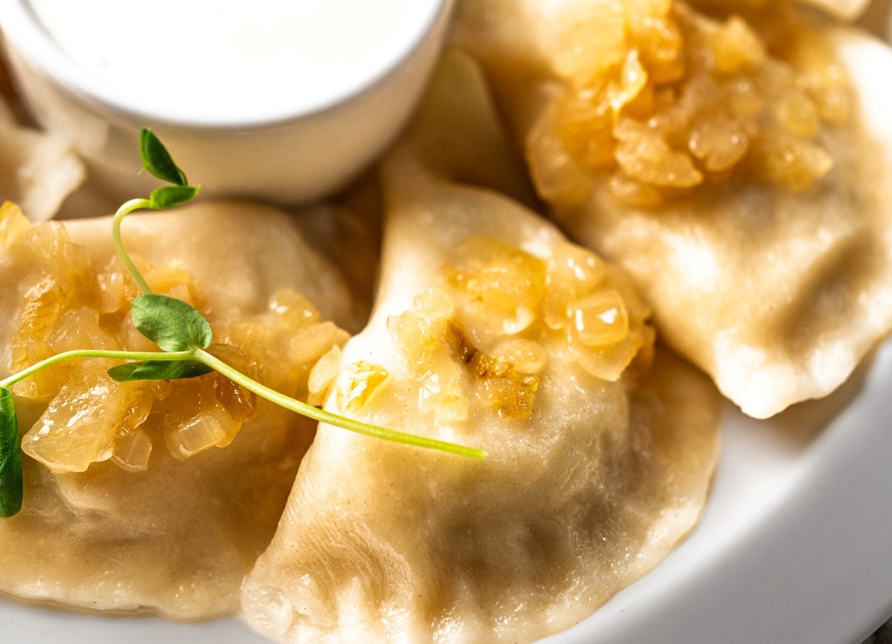 Pierogi z karmelizowaną cebulą i mikrozieleniną, podane z miseczką kwaśnej śmietany na białym talerzu