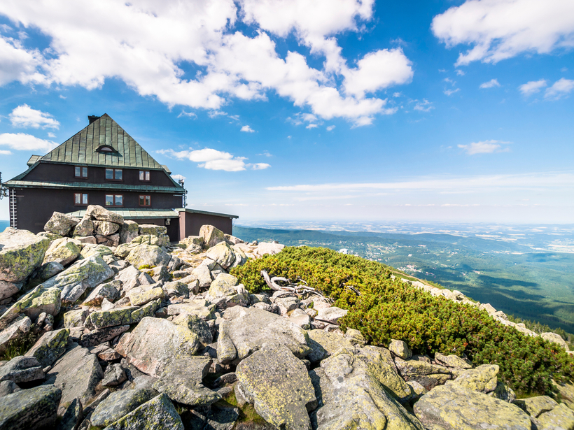 Górskie schronisko na skalistym szczycie, taras z panoramicznym widokiem na doliny i błękitne niebo.