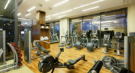 Nowoczesna siłownia hotelowa z widokiem na zewnętrzne okna, wyposażona w bieżnie, rowerki treningowe i sprzęt do ćwiczeń siłowych