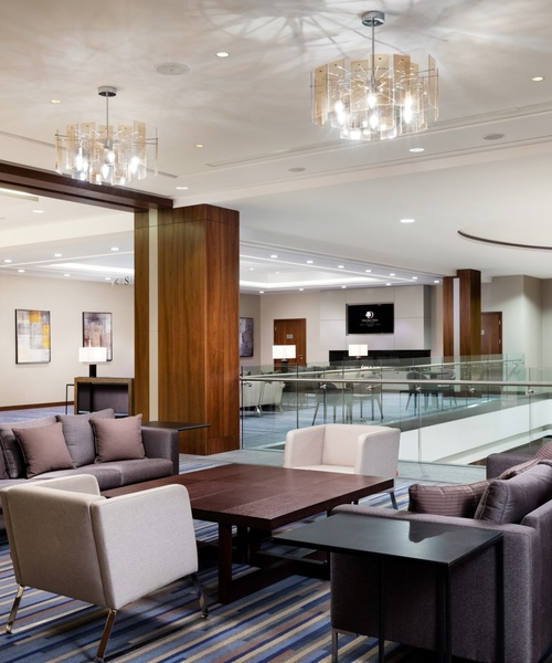 Nowoczesna przestrzeń lobby hotelowego z wygodnymi kanapami, fotelami, dekoracyjnym oświetleniem i kolorowym wieszakiem ściennym.