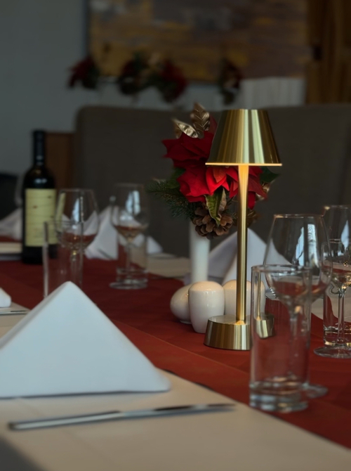 Elegancko nakryty stół w restauracji hotelowej z lampką stołową i świąteczną dekoracją z czerwonymi kwiatami