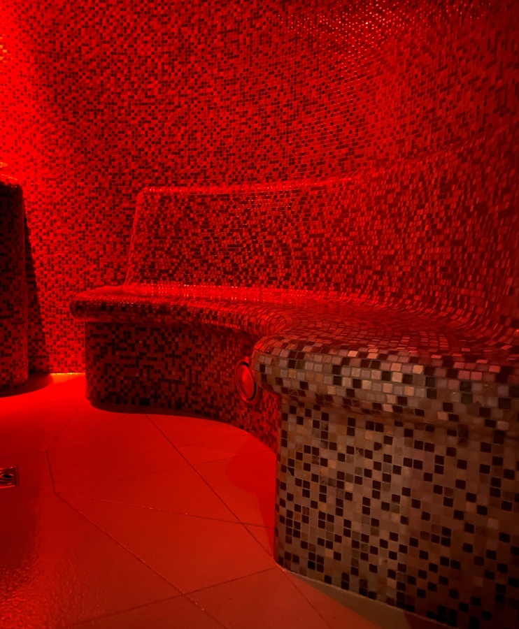 Oświetlona na czerwono mozaikowa ławeczka w relaksującym pokoju spa z podłogą z płytek.