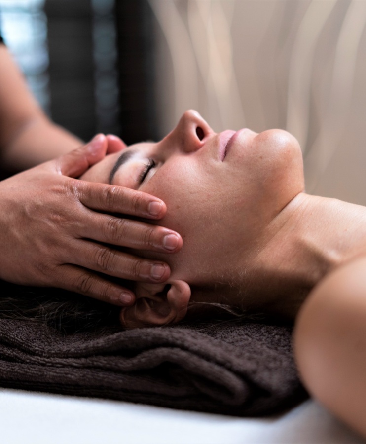 Gość relaksuje się podczas masażu twarzy w spokojnym spa hotelowym, leżąc na ciemnym ręczniku.