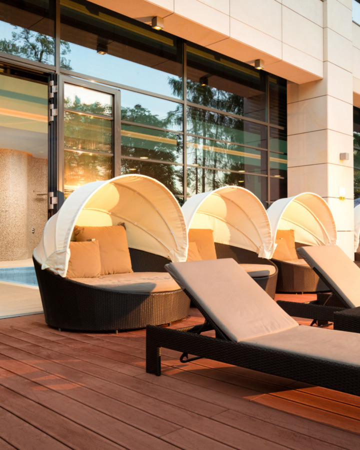 Eleganckie zewnętrzne leżanki i okrągłe kanapy z osłonami przeciwsłonecznymi na tarasie hotelowym z dużymi oknami