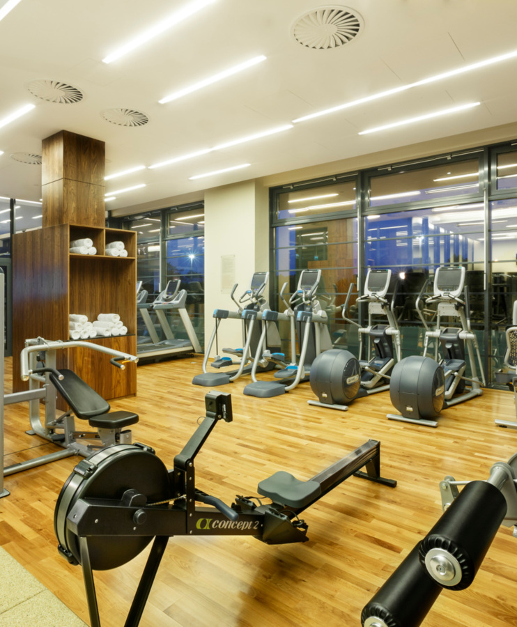 Nowoczesna siłownia hotelowa z widokiem na zewnętrzne okna, wyposażona w bieżnie, rowerki treningowe i sprzęt do ćwiczeń siłowych