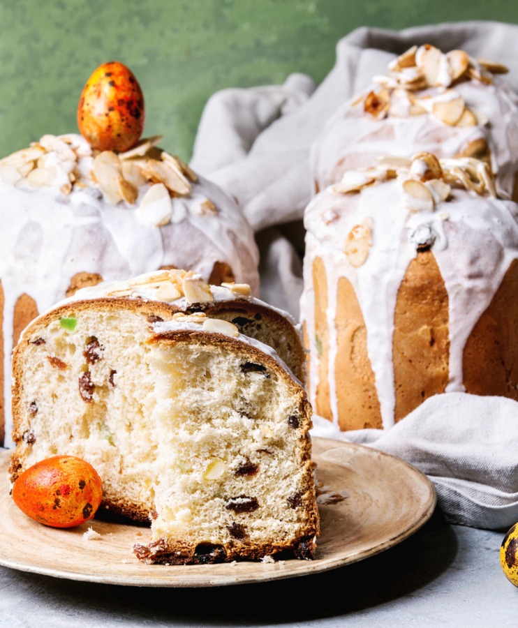 Kawałki tradycyjnego ciasta wielkanocnego z lukrem i migdałami, ozdobione kolorowymi pisankami na talerzu