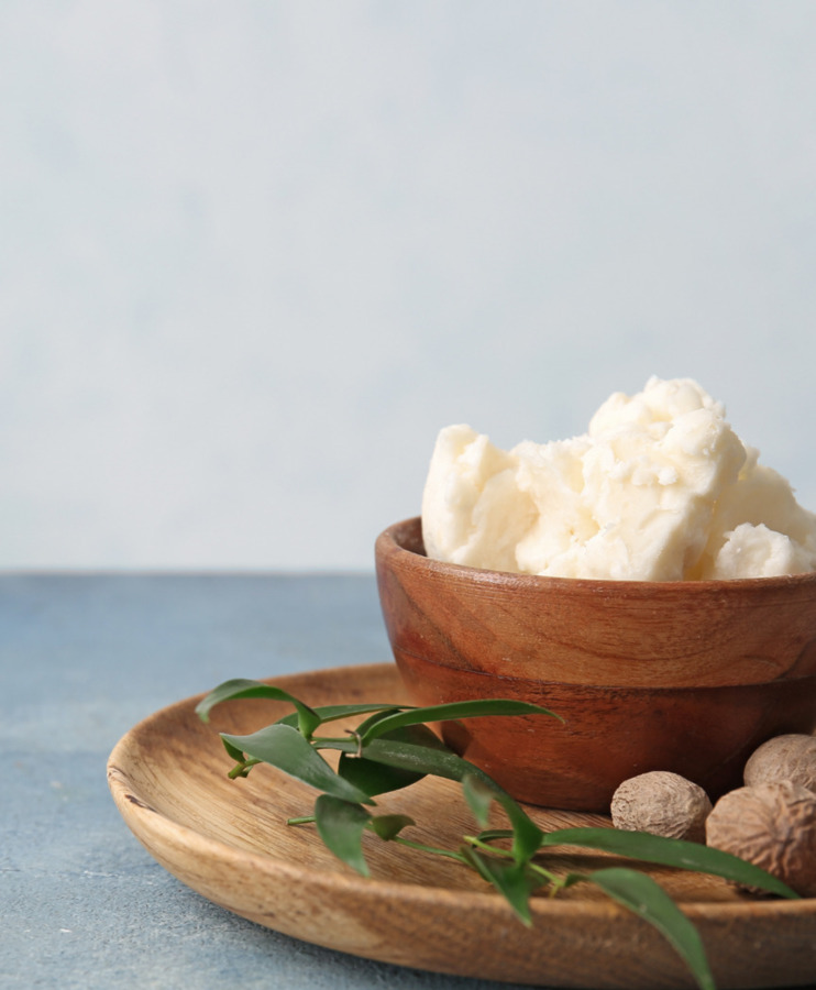 Miseczka masła shea na drewnianej tacy z zielonymi liśćmi i orzechami, naturalny składnik spa lub pielęgnacji ciała