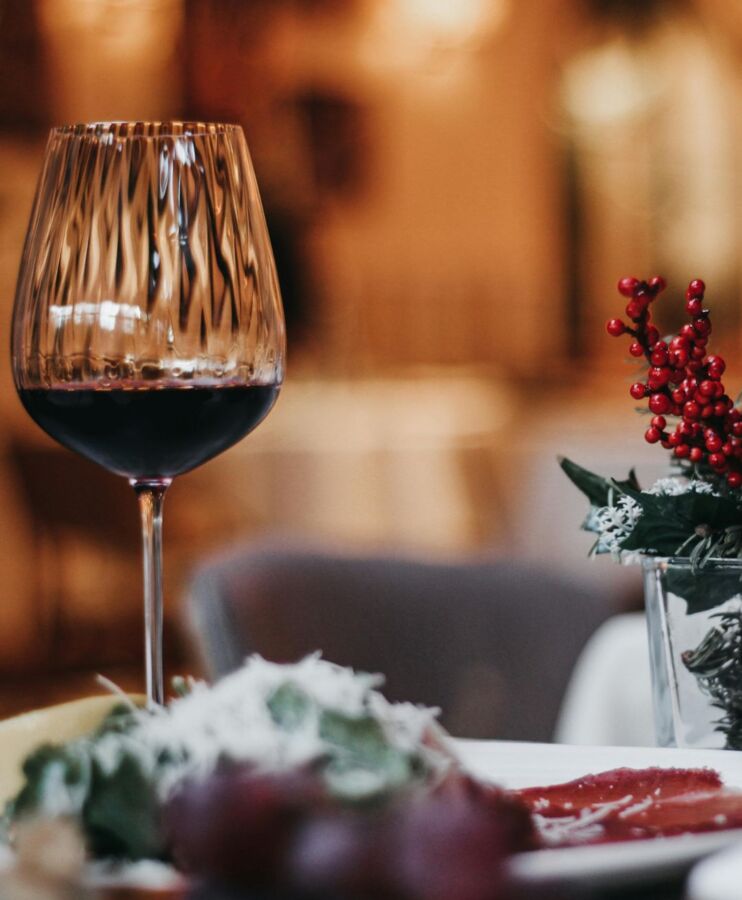Kieliszek czerwonego wina na elegancko nakrytym stole z dekoracją sezonową i rozmytym tłem restauracji.