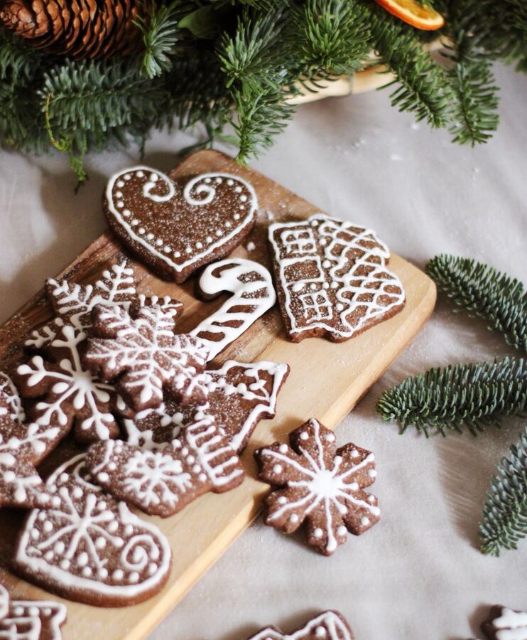 Świąteczne pierniki z białym lukrem w kształcie serc, gwiazdek i chatki, na drewnianej desce z zielonymi gałązkami świerku