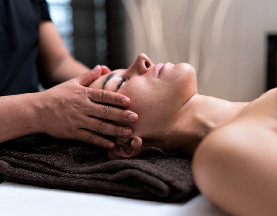 Gość relaksuje się podczas masażu twarzy w spokojnym spa hotelowym, leżąc na ciemnym ręczniku.