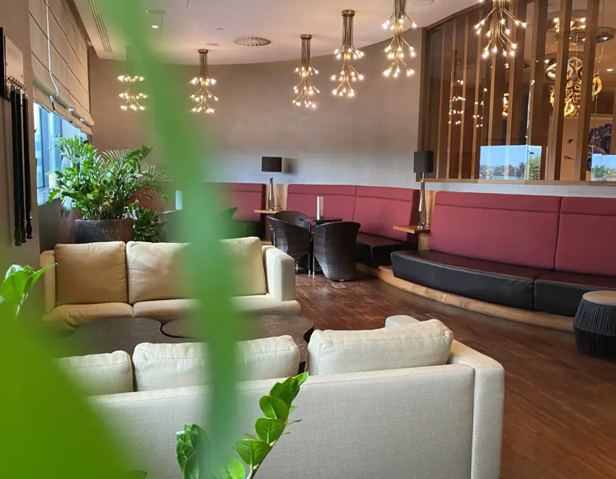 Cozy hotel lounge with beige sofas, burgundy benches, wooden tables, and decorative ceiling lights creating a warm atmosphere