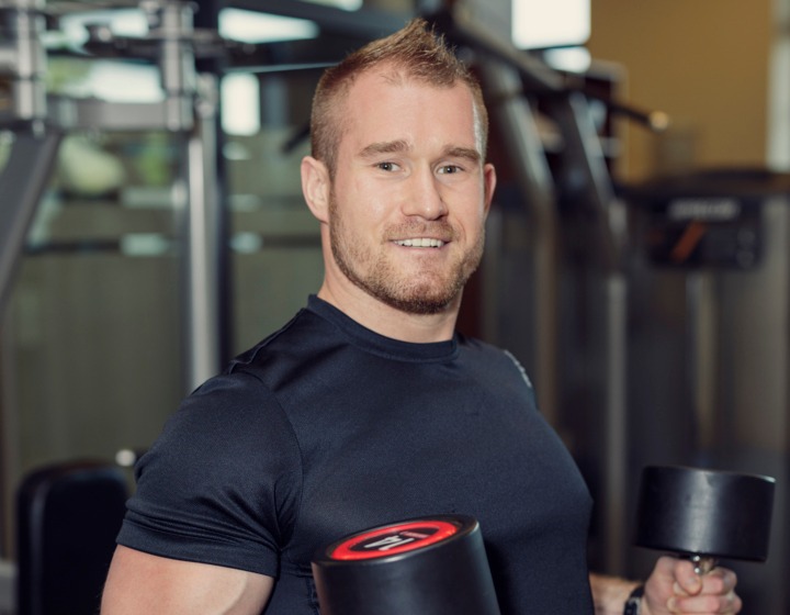 Mężczyzna ćwiczy na siłowni hotelowej, trzyma ciężarki, w otoczeniu nowoczesnego sprzętu fitness.