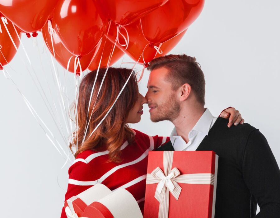 Para obejmująca się romantycznie, trzyma sercowe balony i prezenty w czerwonych pudełkach na świętowanie w hotelu.