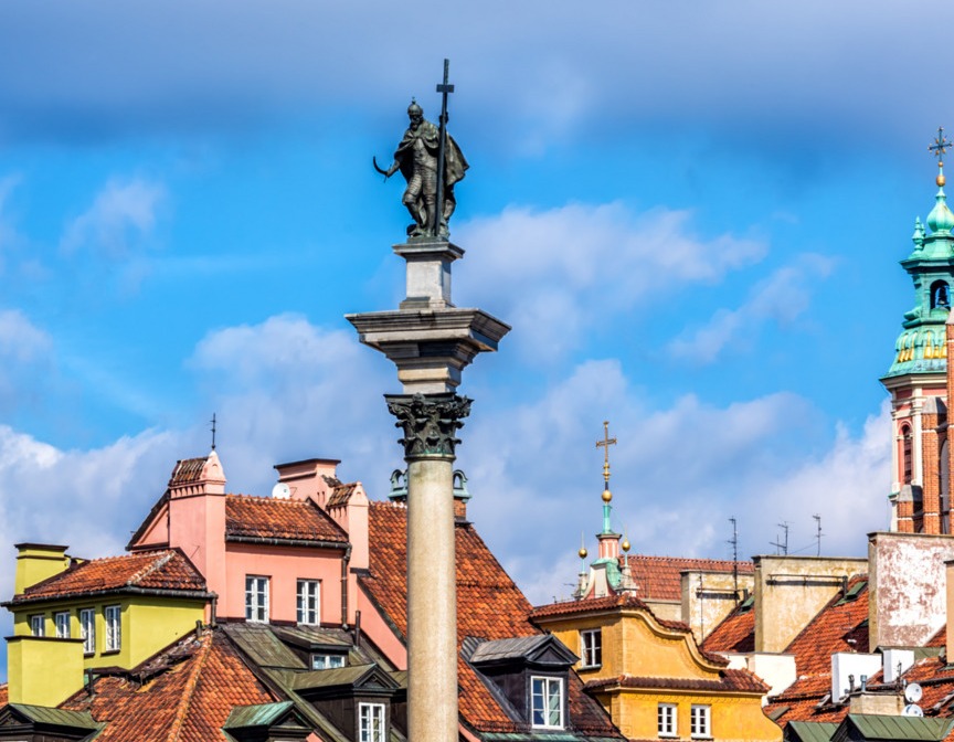 Kolumna Zygmunta w centrum Warszawy na tle kolorowych kamienic z ceglanymi dachami pod błękitnym niebem