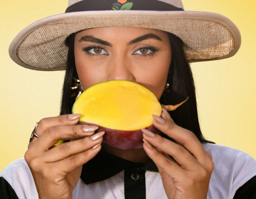 Woman wearing a straw hat holding a ripe mango half, ready to enjoy the fresh, juicy fruit.