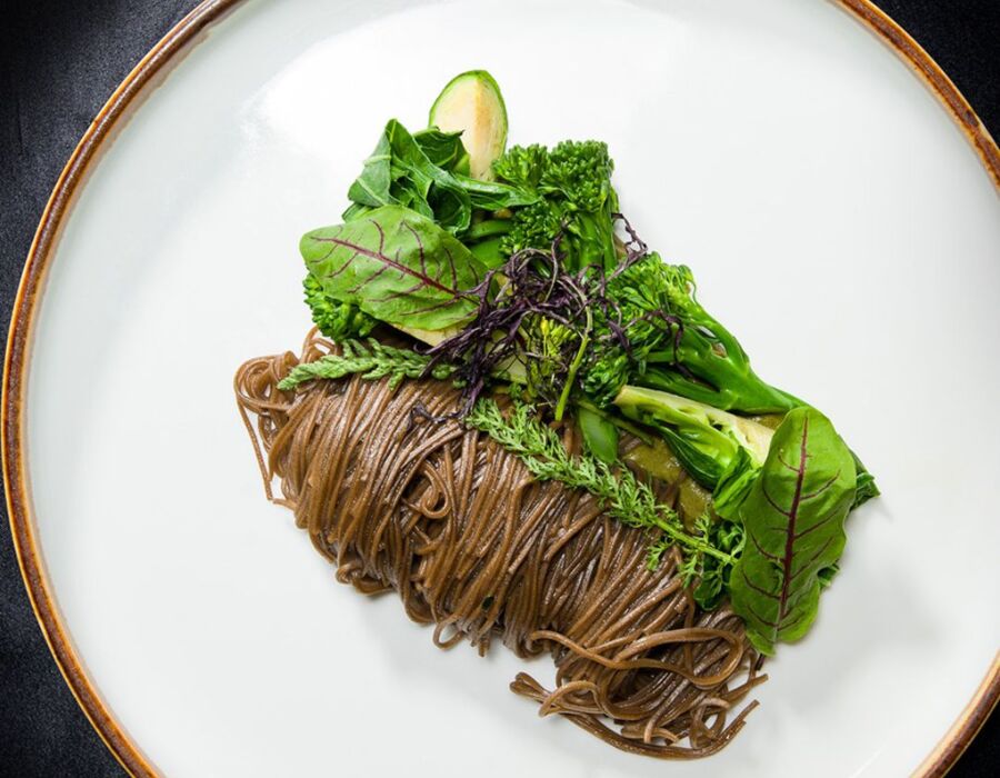 Delikatne makaron soba podane z mieszanką świeżych zielonych warzyw na eleganckim talerzu.