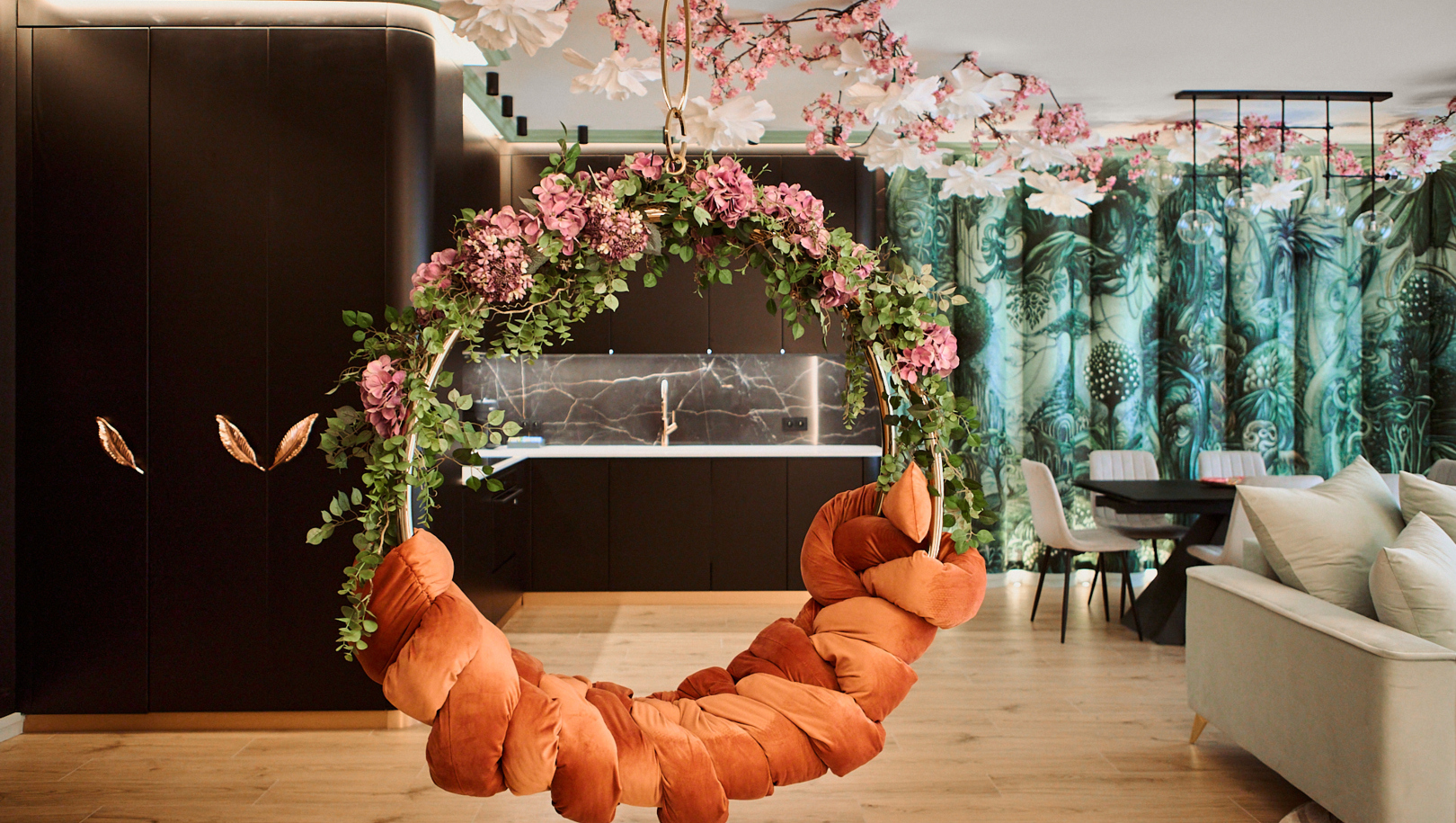 Wisząca okrągła huśtawka z kwiatami i pluszowymi rdzawymi poduszkami w apartamencie z aneksem i jadalnią