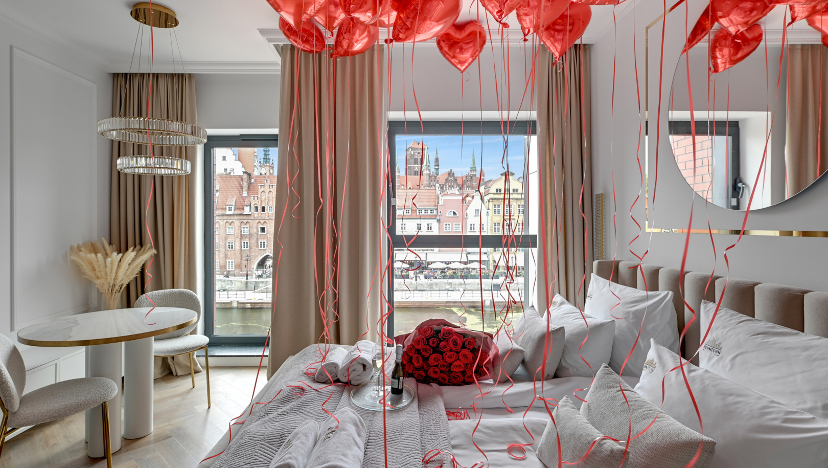 Romantyczny pokój deluxe z czerwonymi balonami w kształcie serc, bukietem czerwonych róż i szampanem na łóżku, widok na rzekę i starówkę