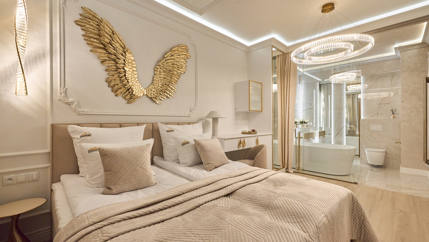 Luksusowy apartament w neutralnych tonach z łóżkiem king, złotymi skrzydłami na ścianie, szklaną marmurową łazienką i wolnostojącą wanną.