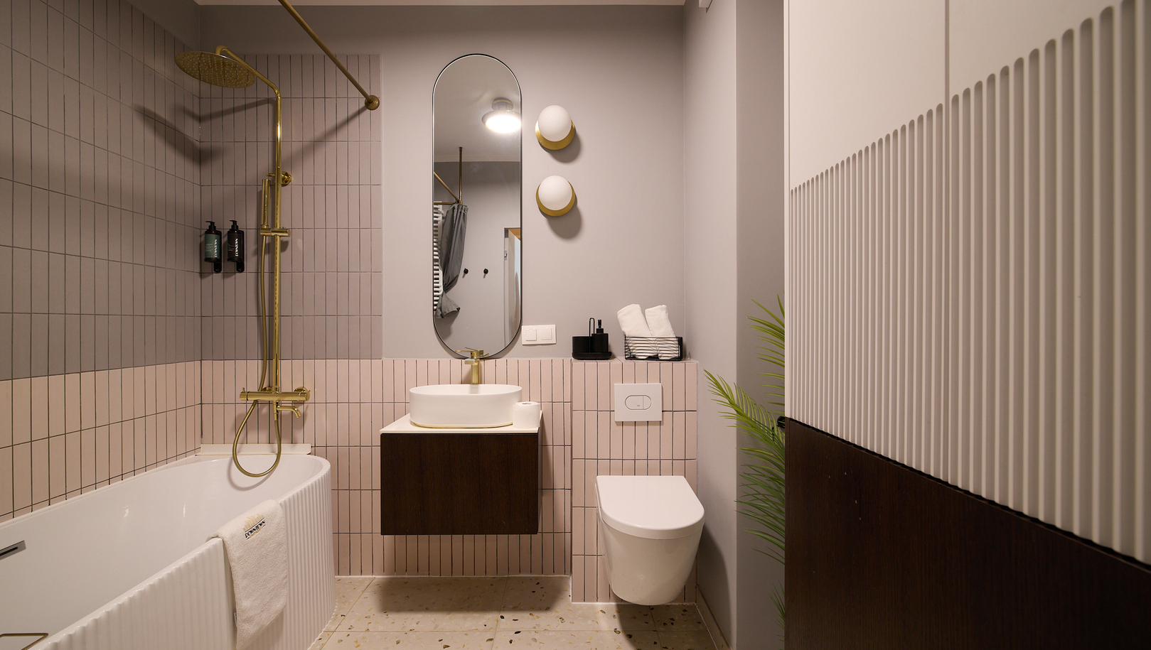 Nowoczesna łazienka hotelowa z wanną, złotą deszczownicą, podwieszanym blatem z umywalką, owalnym lustrem i wiszącą toaletą