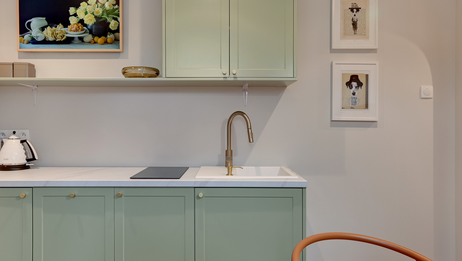 Aneks kuchenny w apartamencie z miętowymi szafkami, marmurowym blatem, mosiężną baterią, płytą indukcyjną, czajnikiem i oprawionymi obrazami