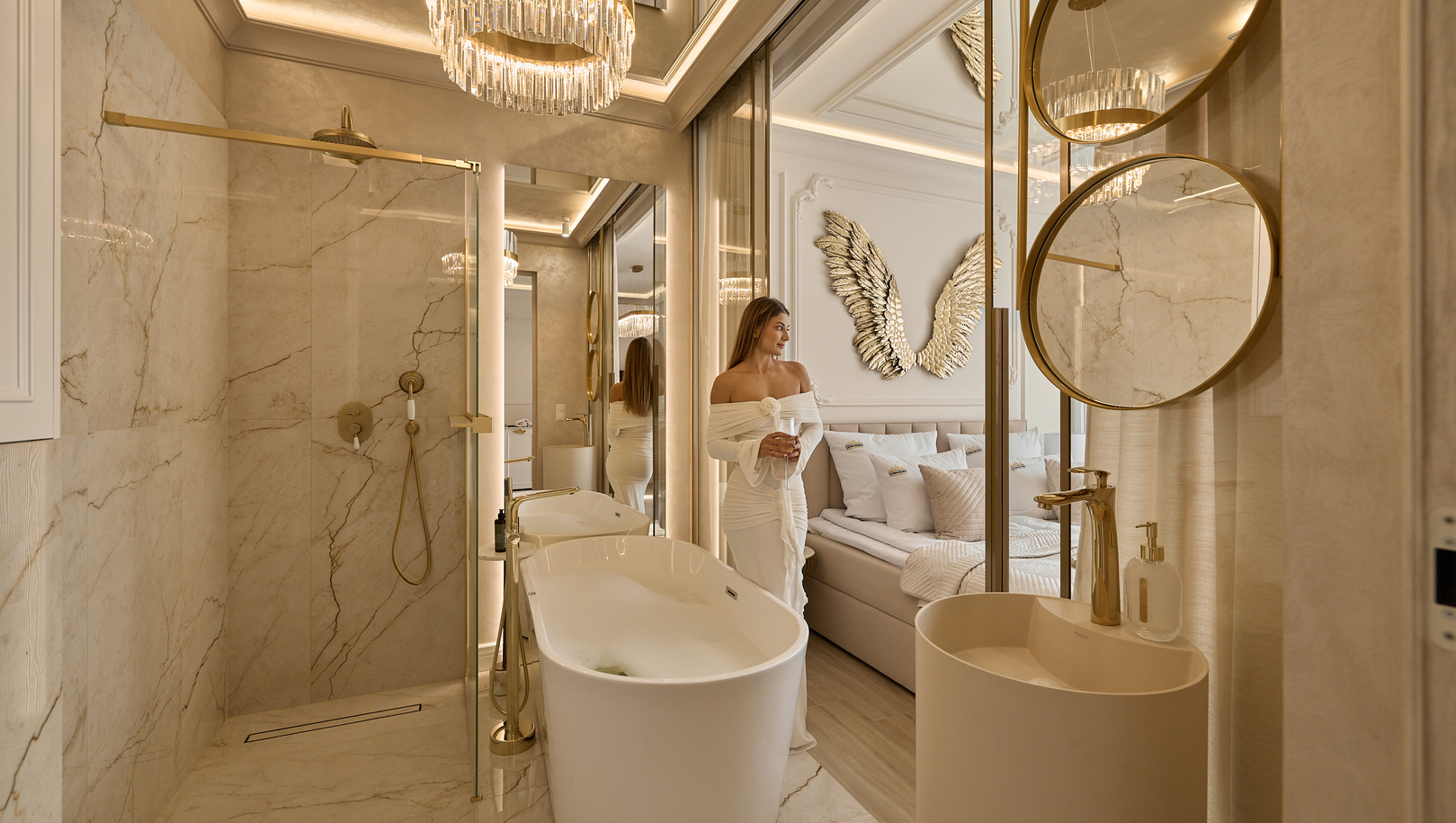 Luksusowa łazienka w apartamencie z wolnostojącą wanną, marmurową kabiną, złotymi armaturami, żyrandolem i gościem z drinkiem.