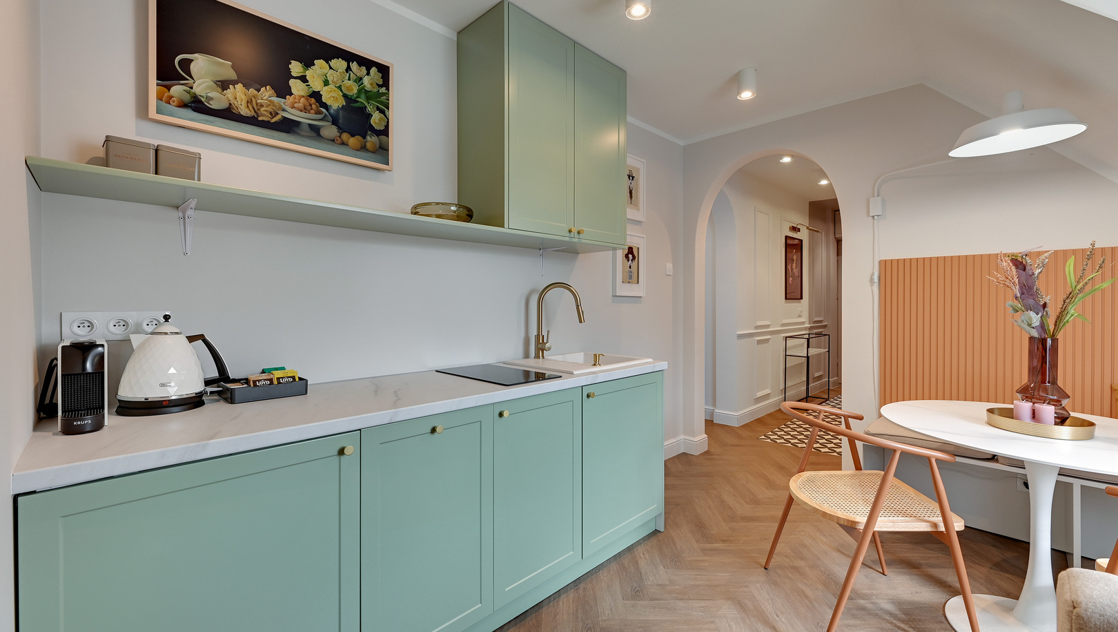 Kuchnia w kolorze miętowym z marmurowym blatem, złotą baterią, ekspresem do kawy i czajnikiem; okrągły stół, nowoczesne krzesła i wazon