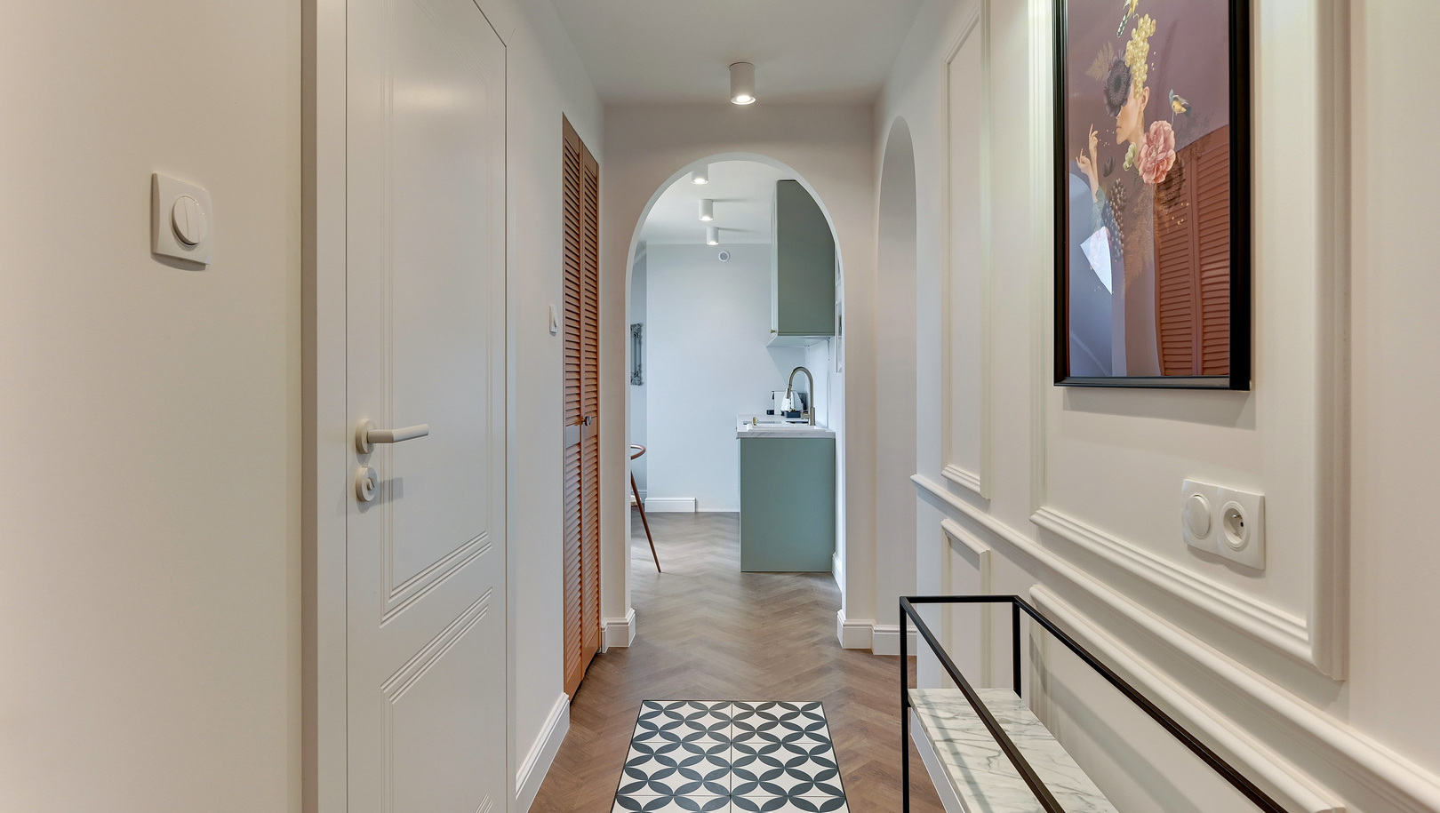 Jasny butikowy korytarz z łukowym przejściem, podłogą w jodełkę, wzorzystym dywanikiem, marmurową konsolą i aneksem kuchennym