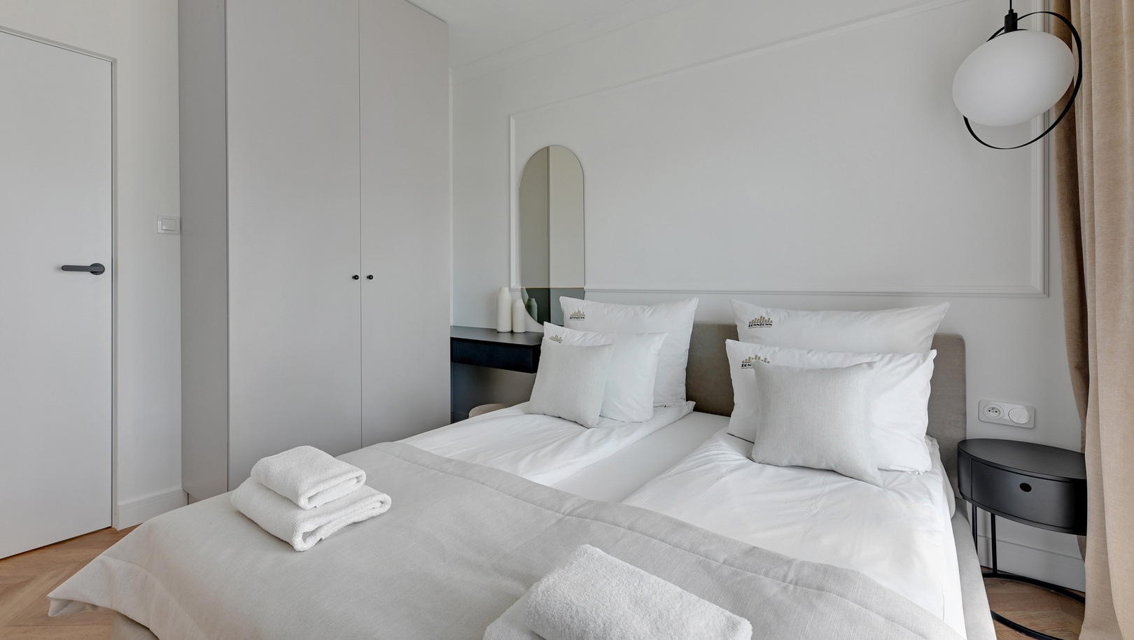 Jasny nowoczesny pokój z dwoma złączonymi łóżkami, świeżą białą pościelą, złożonymi ręcznikami, szafą, stolikiem nocnym i lampą wiszącą