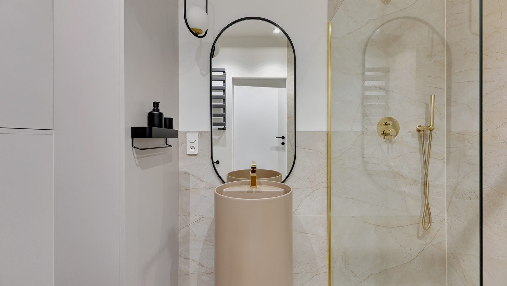 Nowoczesna łazienka hotelowa z wolnostojącą umywalką, owalnym lustrem, marmurowymi płytkami i złotym prysznicem