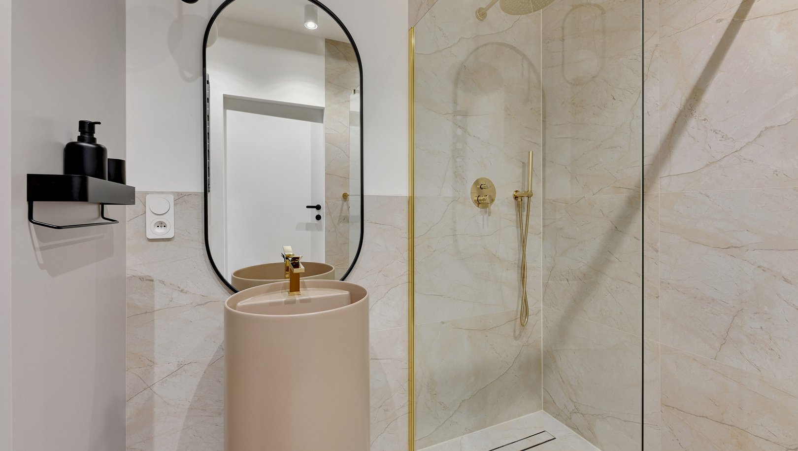 Nowoczesna łazienka z marmurem, przeszklonym prysznicem ze złotą deszczownicą i słuchawką, wolnostojąca umywalka i owalne lustro.