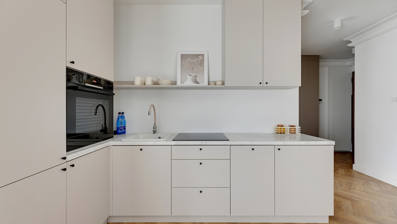 Nowoczesny aneks kuchenny z marmurowym blatem, płytą indukcyjną, wbudowanym piekarnikiem, zlewem, jasnymi szafkami i podłogą w jodełkę