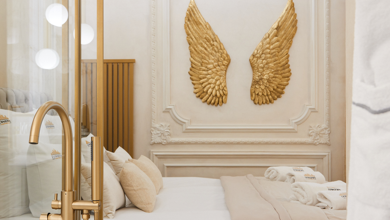 Luksusowy apartament z neutralną pościelą, miękkimi poduszkami, zwiniętymi ręcznikami, złotymi skrzydłami na ścianie i złotą armaturą