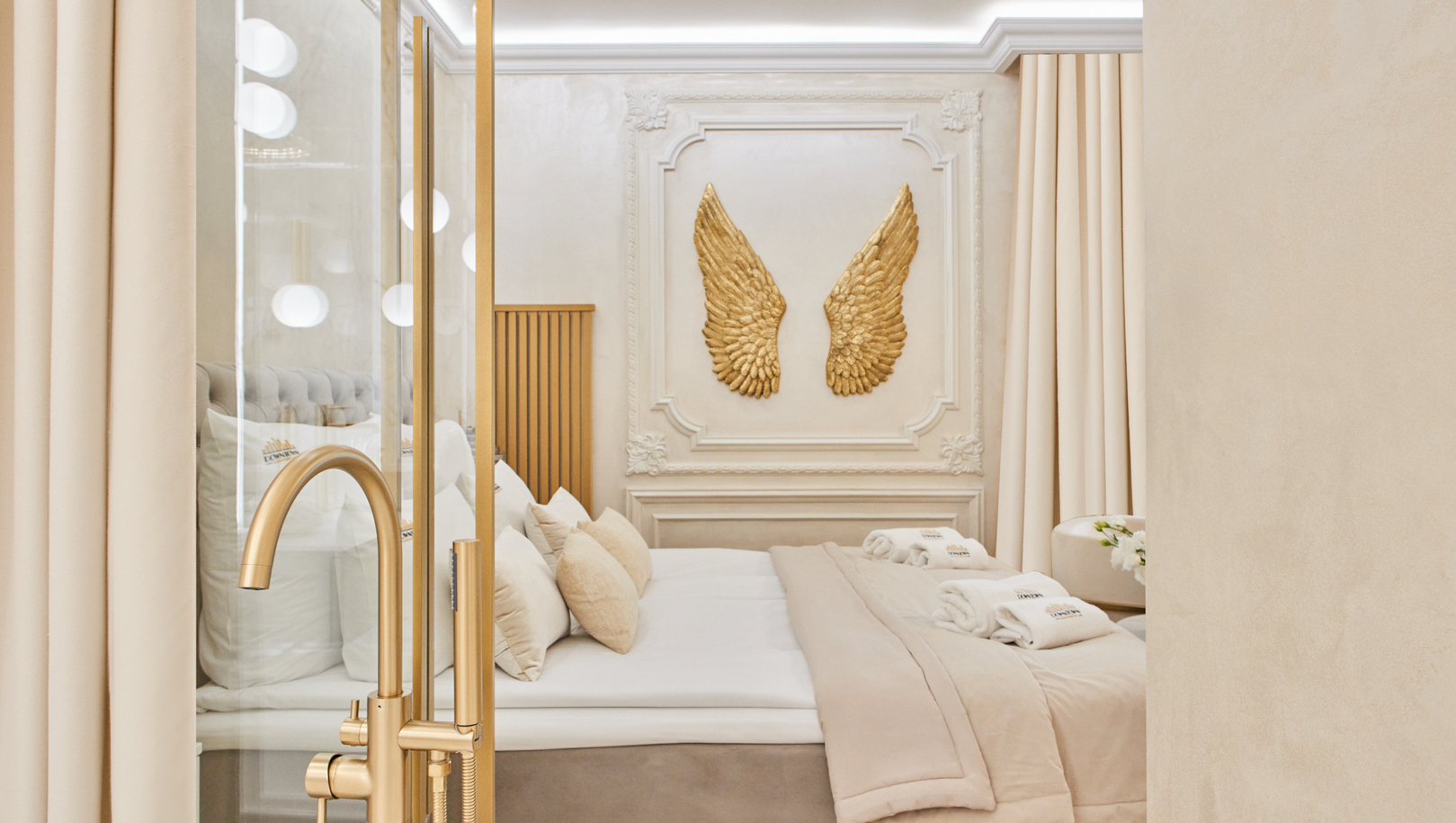 Elegancki pokój butikowy z ozdobną sztukaterią i złotymi skrzydłami, przytulnym łóżkiem, neutralną pościelą, ręcznikami i złotym kranem.