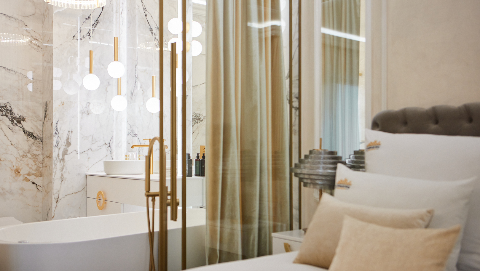 Luksusowy apartament z wolnostojącą wanną, marmurową łazienką, złotymi armaturami i kulistymi lampami za szklaną ścianką, przytulne łóżko.