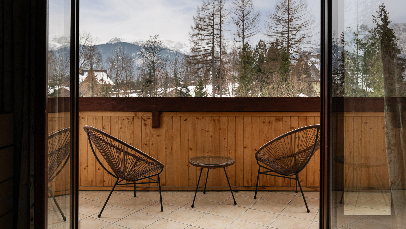 Prywatny balkon z dwiema plecionymi krzesłami i stolikiem, drewniana balustrada, widok na ośnieżone góry