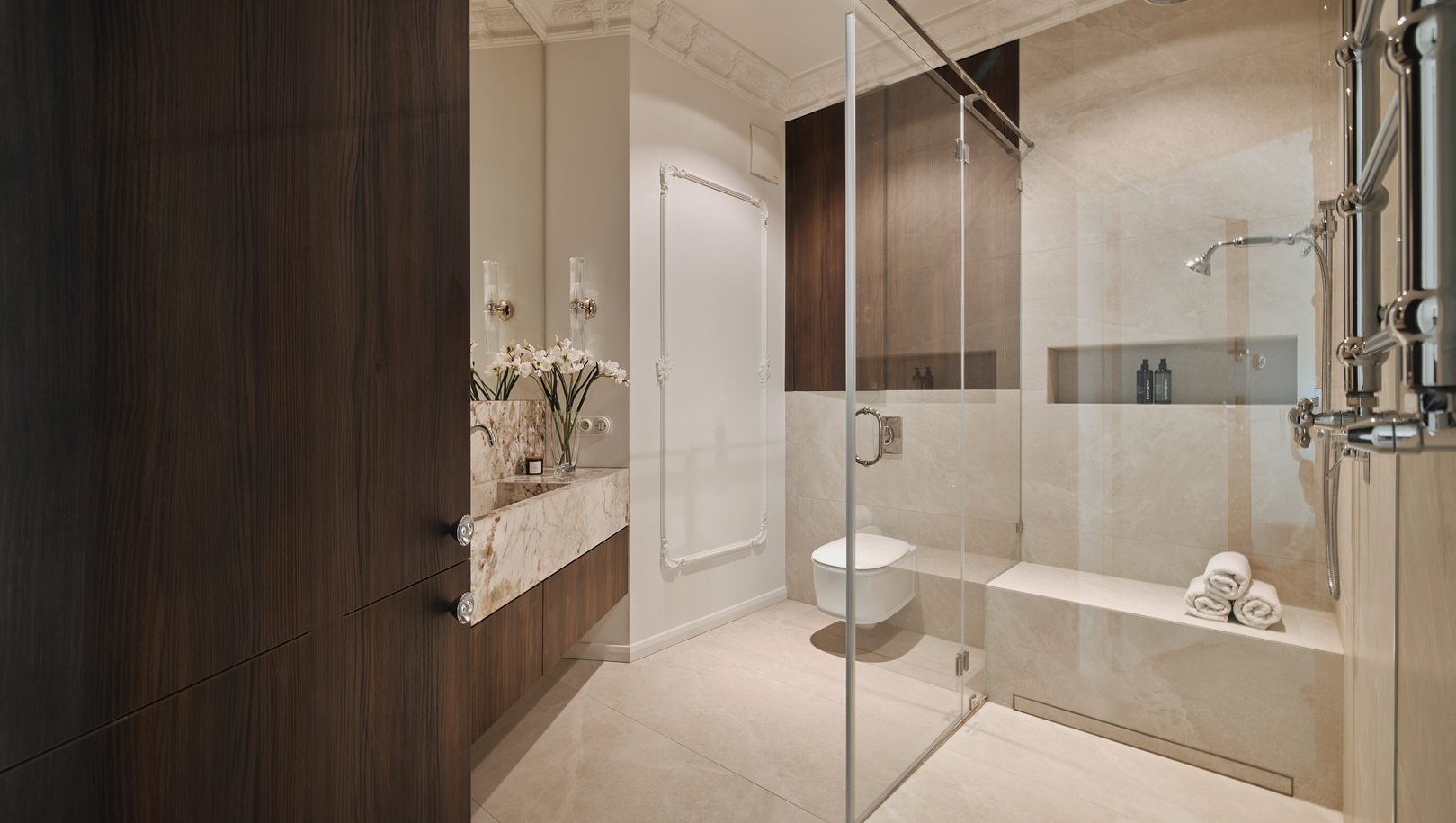 Luksusowa łazienka hotelowa z marmurową umywalką, ciemnym drewnem, szklaną kabiną prysznicową, deszczownicą i ręcznikami.