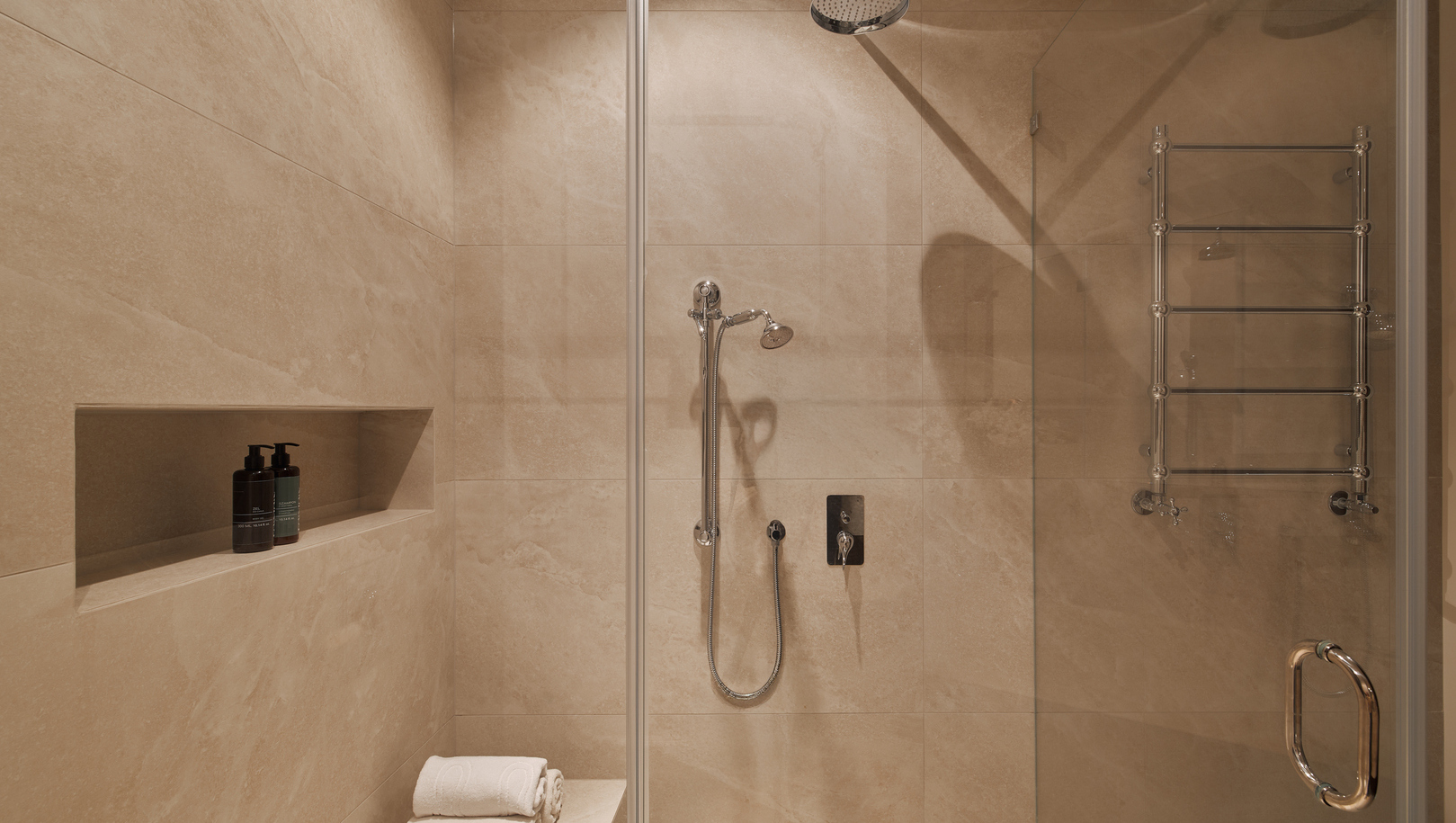 Kabina prysznicowa w stylu spa z deszczownicą i słuchawką, płytki marmurowe, wnęka z kosmetykami i złożonymi ręcznikami