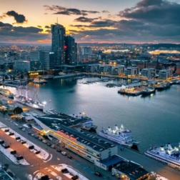 Wieczorny widok na oświetlony port i marinę z promami, nadbrzeżną promenadą ze śniegiem i nowoczesnymi wieżowcami.