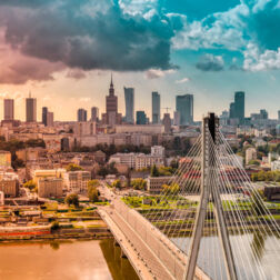 Nadbrzeżna panorama z mostem wantowym, nowoczesnymi wieżowcami i zabytkową wieżą pod dramatycznym zachodem słońca.