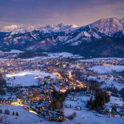 Górska wioska ośnieżona o zmierzchu z drewnianymi willami, migoczącymi światłami i potężnymi, zaśnieżonymi szczytami