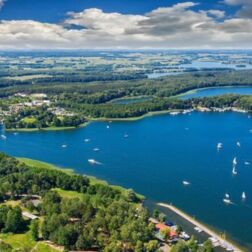 Widok z lotu ptaka na ośrodek nad jeziorem z wyspami, przystanią i żaglówkami otoczony lasami